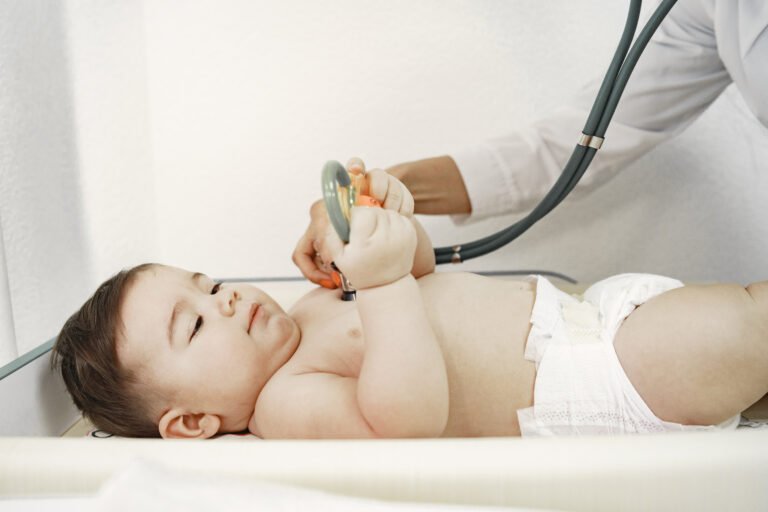 Pediatrician in a white coat examines baby with a stethoscope