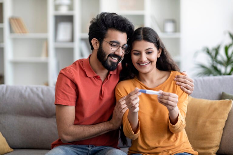 Portrait Of Happy Young Indian Couple Holding Positive Pregnancy Test At Home